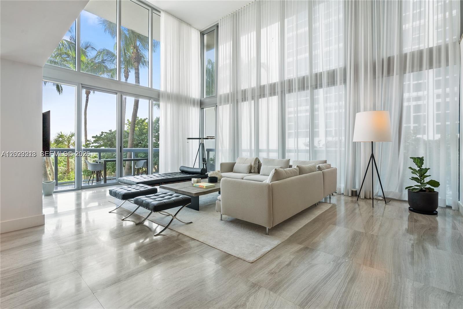 A modern living room features floor-to-ceiling windows, light-colored tile floors, and a neutral sofa — 6899 Collins Ave # 202, Miami Beach FL 33141, MIAMI BEACH, FL