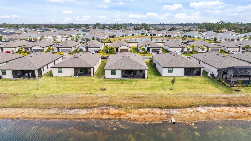 An aerial view shows three suburban houses with paved driveways and a pond in the background — 1505 SADDLEWOOD CIRCLE, PORT CHARLOTTE, FL