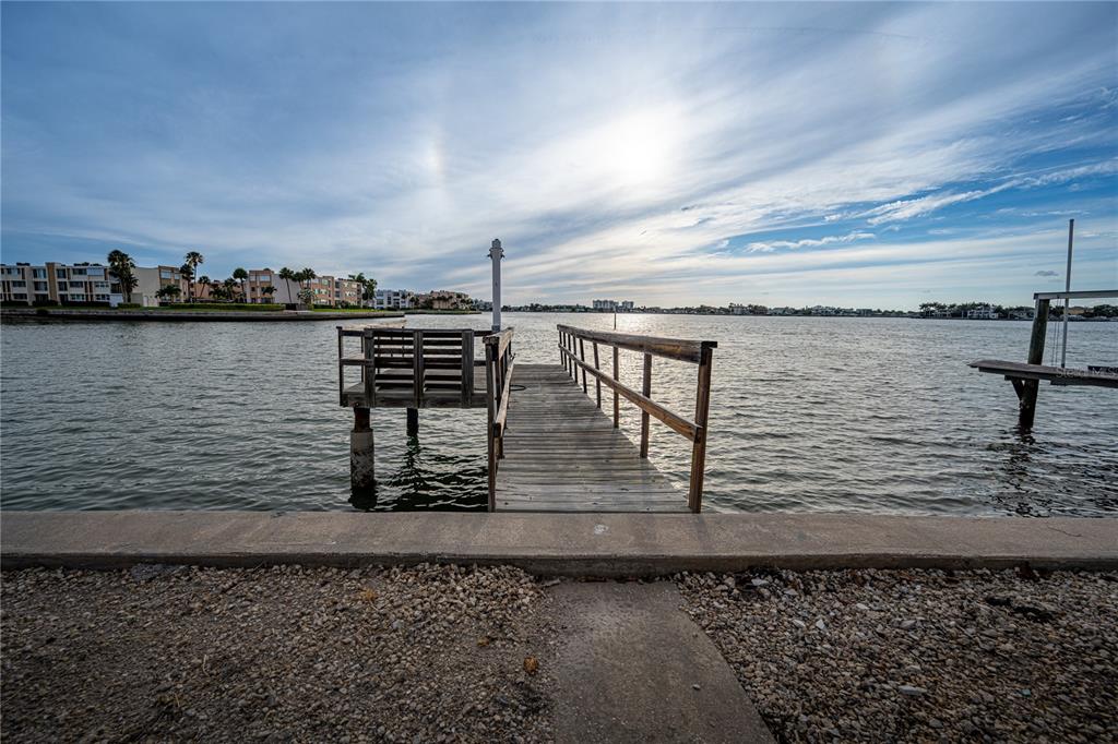 A wooden dock extends into a calm bay under a bright, cloudy sky — 1425 COREY WAY S, SOUTH PASADENA, FL
