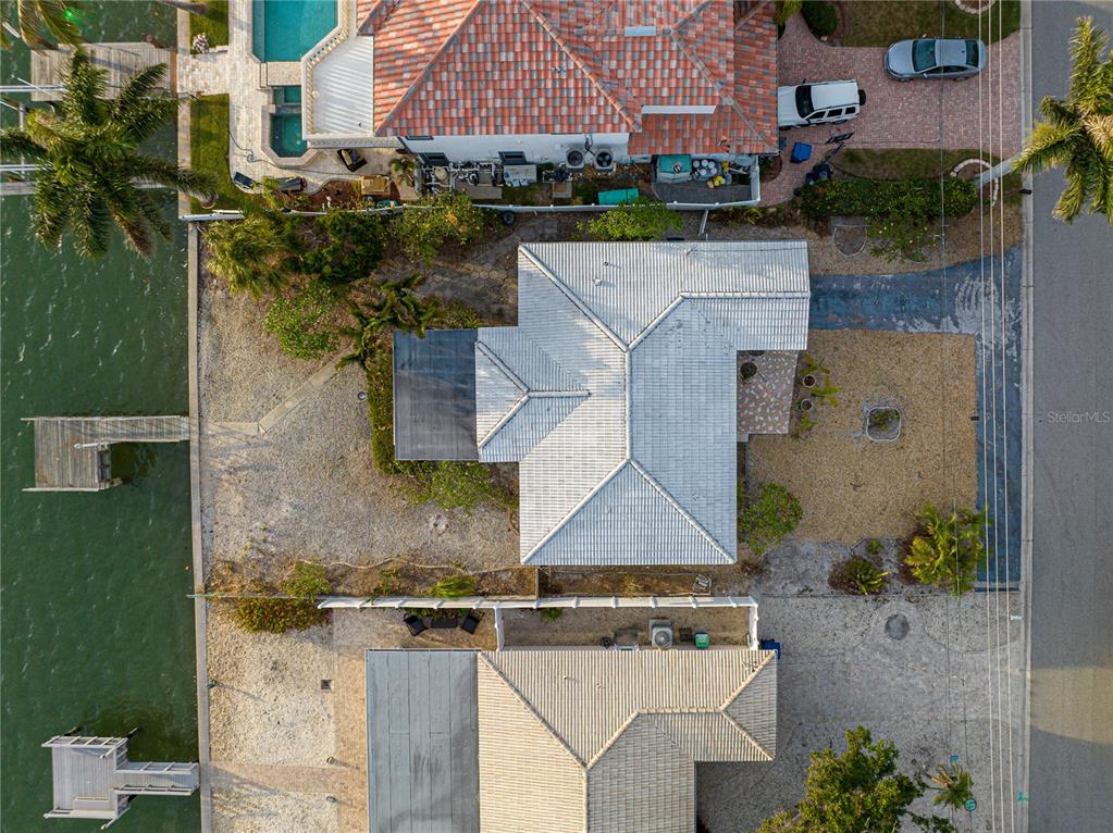An aerial view shows two waterfront houses with tiled roofs, docks, and gravel yards — 1425 COREY WAY S, SOUTH PASADENA, FL