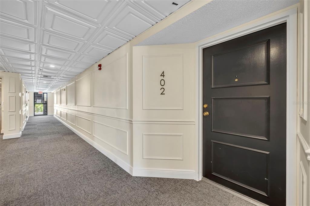 A hallway with gray carpet, white paneled walls, a coffered ceiling, and a black door — 300 CAROLINA AVENUE UNIT 402C, WINTER PARK, FL