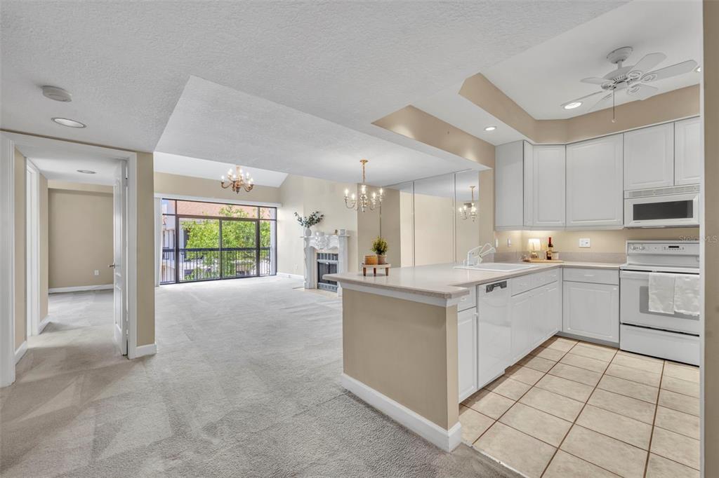 A kitchen with white cabinets and tile flooring overlooks a carpeted living area with a fireplace — 300 CAROLINA AVENUE UNIT 402C, WINTER PARK, FL