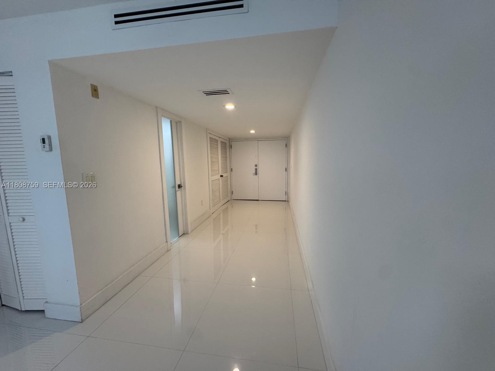 A white hallway features glossy tile flooring, recessed lighting, and several closed doors — 6423 Collins Ave # 1001, Miami Beach FL 33141, MIAMI BEACH, FL