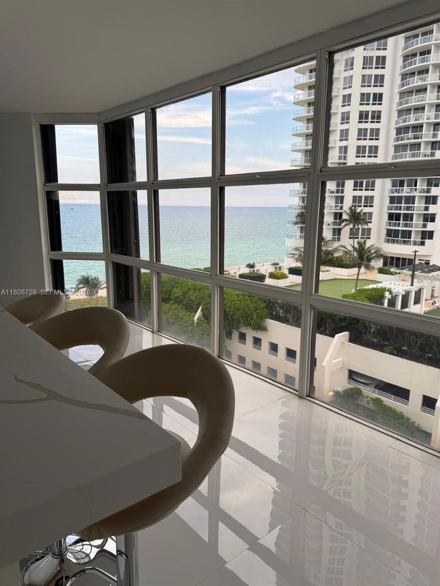 A modern kitchen island with bar stools overlooks the ocean and a neighboring high-rise building — 6423 Collins Ave # 1001, Miami Beach FL 33141, MIAMI BEACH, FL