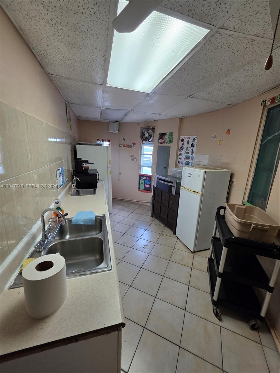 A narrow kitchen features a double sink, white appliances, tiled floors, and a drop ceiling — 2660 SW 17th St, Miami FL 33145, MIAMI, FL