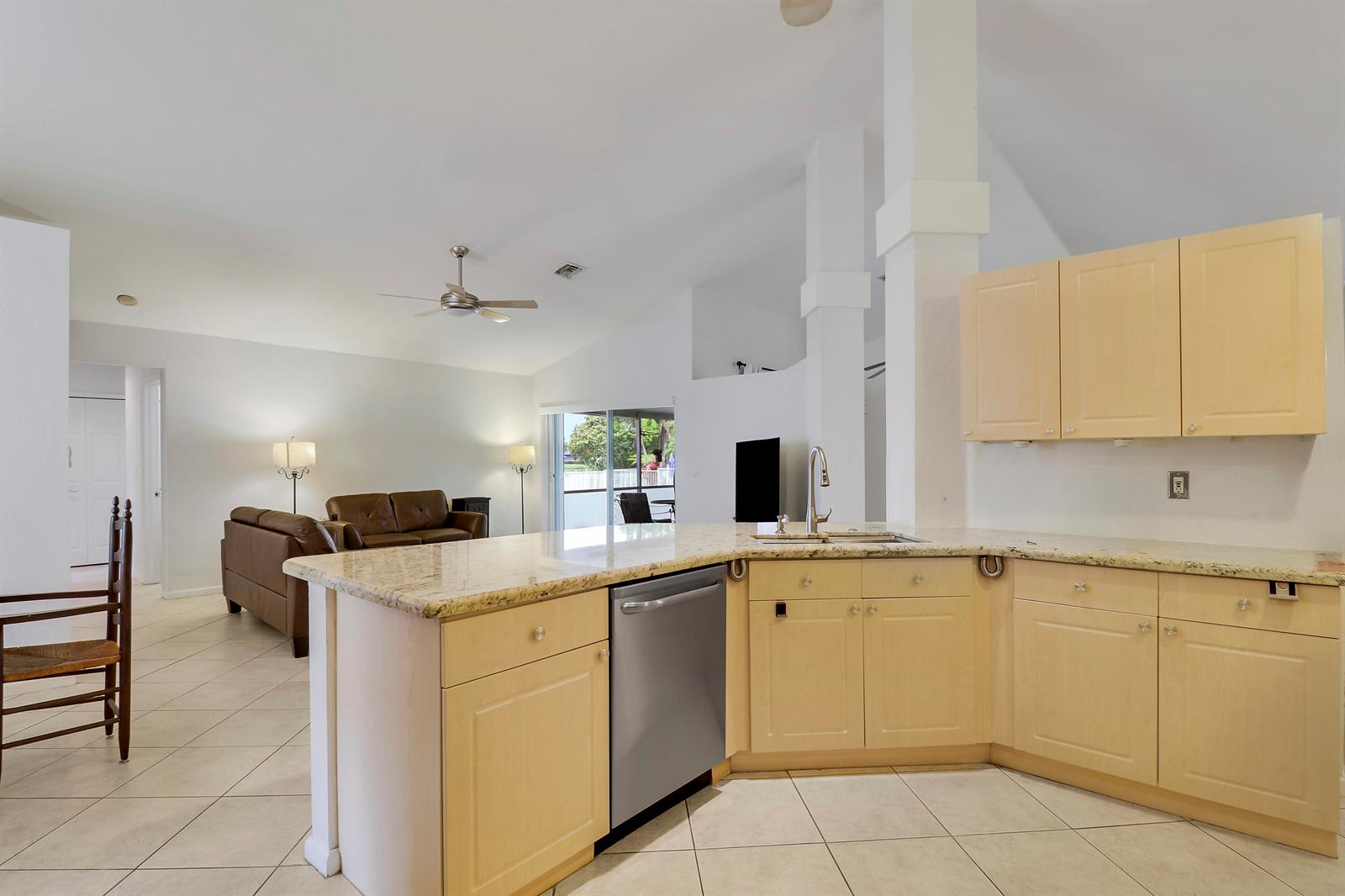 A kitchen with light wood cabinets and granite countertops overlooks an open-concept living area — 7160 Brickyard Circle, Lake Worth FL 33467, LAKE WORTH, FL