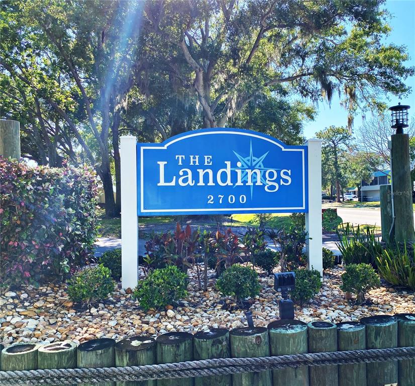 A blue sign for The Landings 2700 stands in a landscaped garden with trees — 2700 NEBRASKA AVENUE UNIT 5-105, PALM HARBOR, FL
