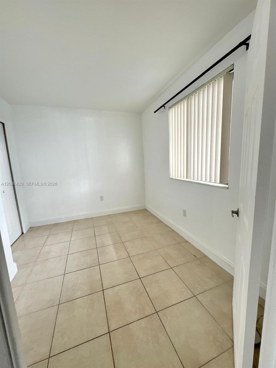 A small, empty room features white walls, beige tile flooring, and a window with blinds — 8275 SW 152nd Ave # 302, Miami FL 33193, MIAMI, FL