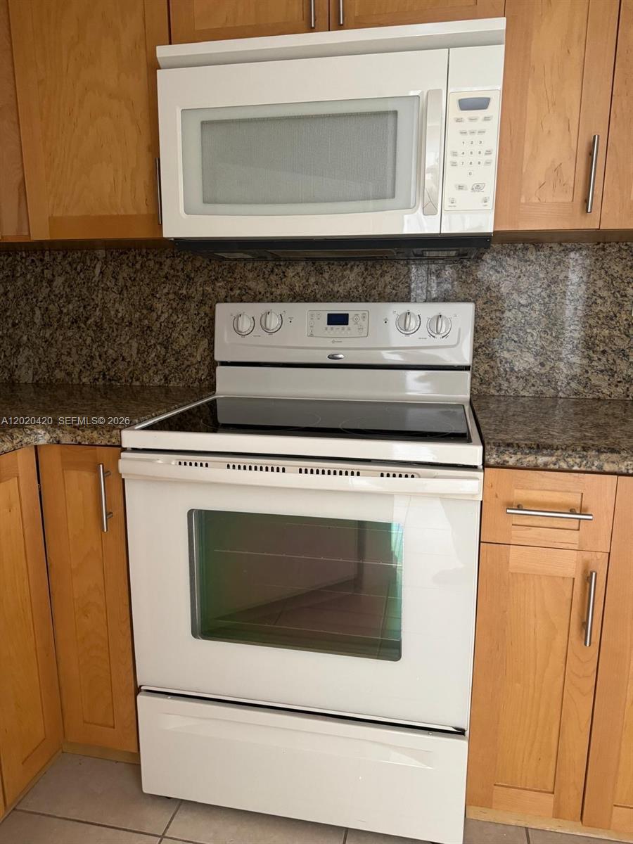 A white electric range and microwave are installed between light wood kitchen cabinets — 8275 SW 152nd Ave # 302, Miami FL 33193, MIAMI, FL