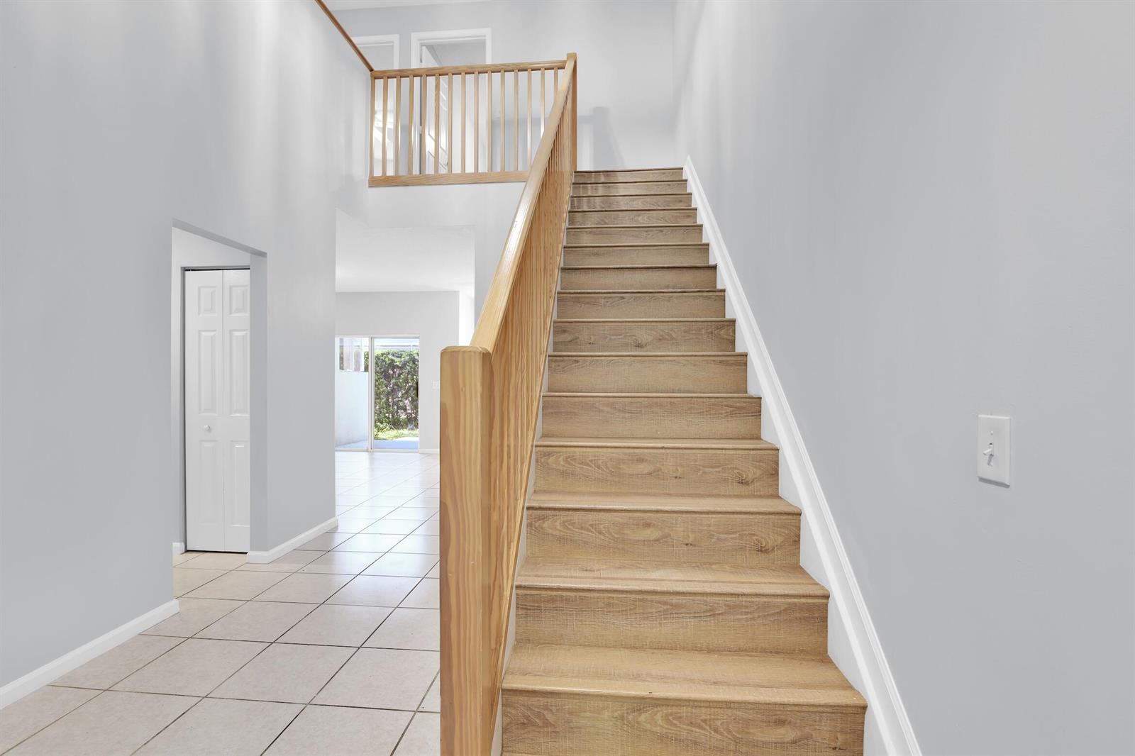 A staircase with wood-look treads and a wooden railing leads to an upper landing — 8297 Via Leonessa, Boca Raton FL 33433, BOCA RATON, FL