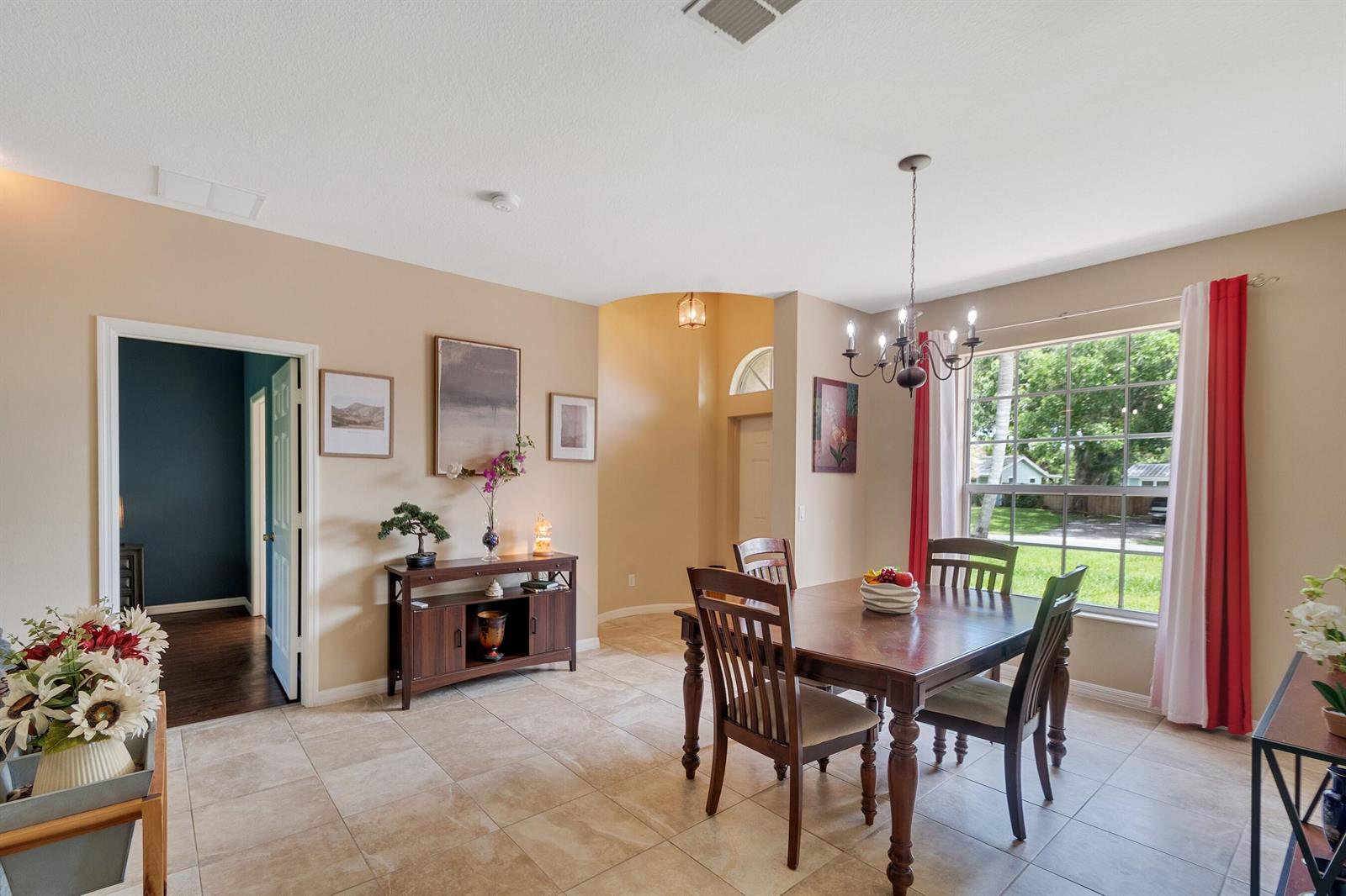 A dining room with tile floors, a wooden table, and a chandelier near a window — SEBASTIAN, FL