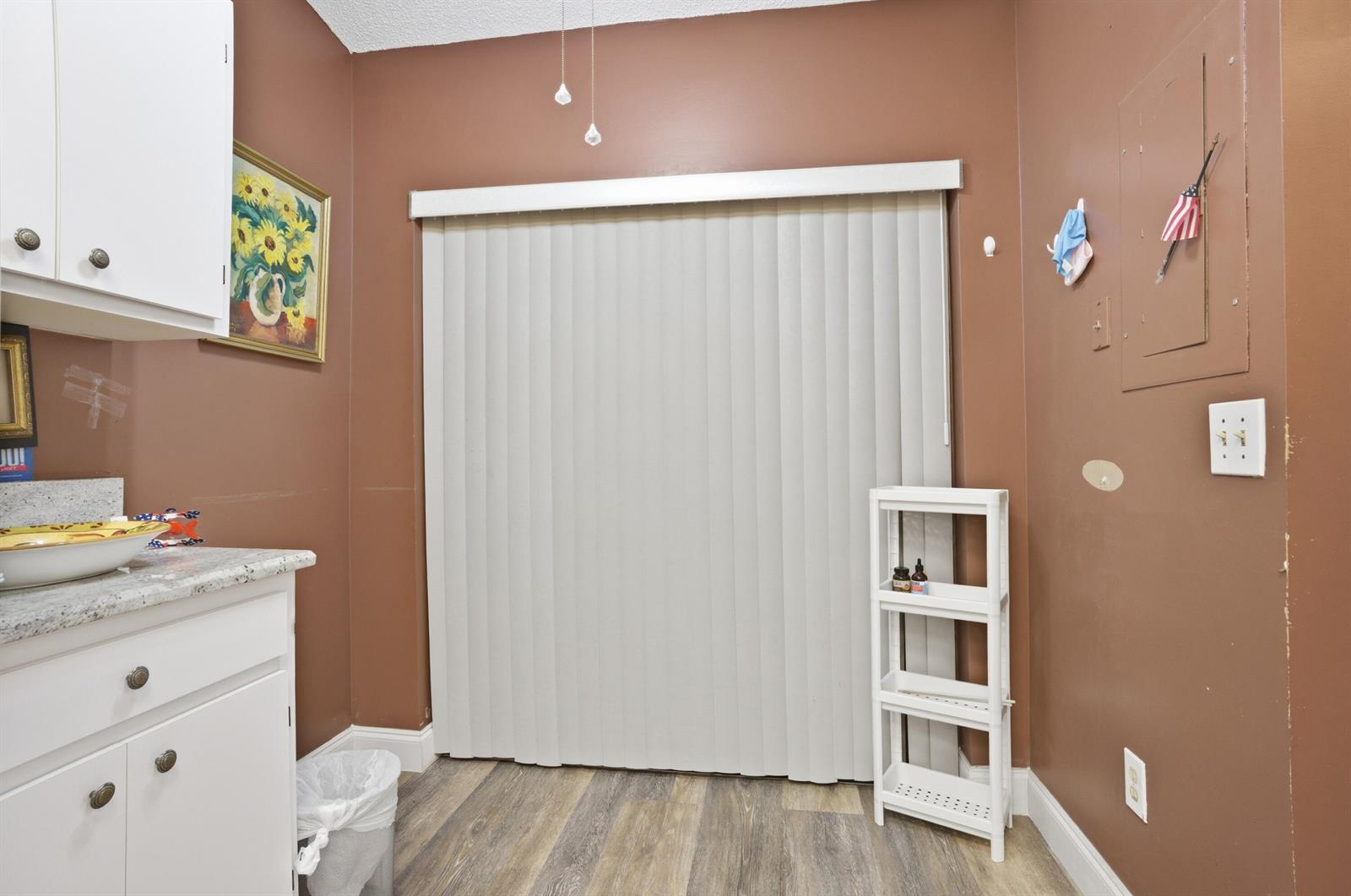 A kitchen area features brown walls, white cabinets, a sliding glass door, and wood-look flooring — 3582 Willa Way # B, Lake Worth FL 33467, LAKE WORTH, FL