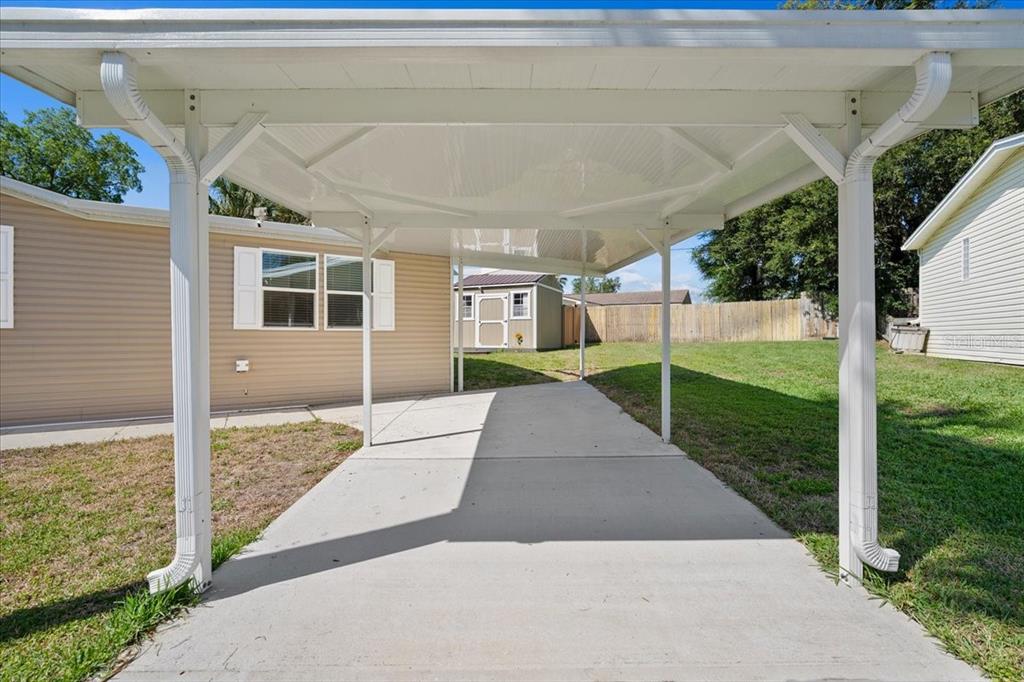 A concrete carport with a white metal roof stands beside a tan mobile home — 1137 YAUPON STREET, DAYTONA BEACH, FL
