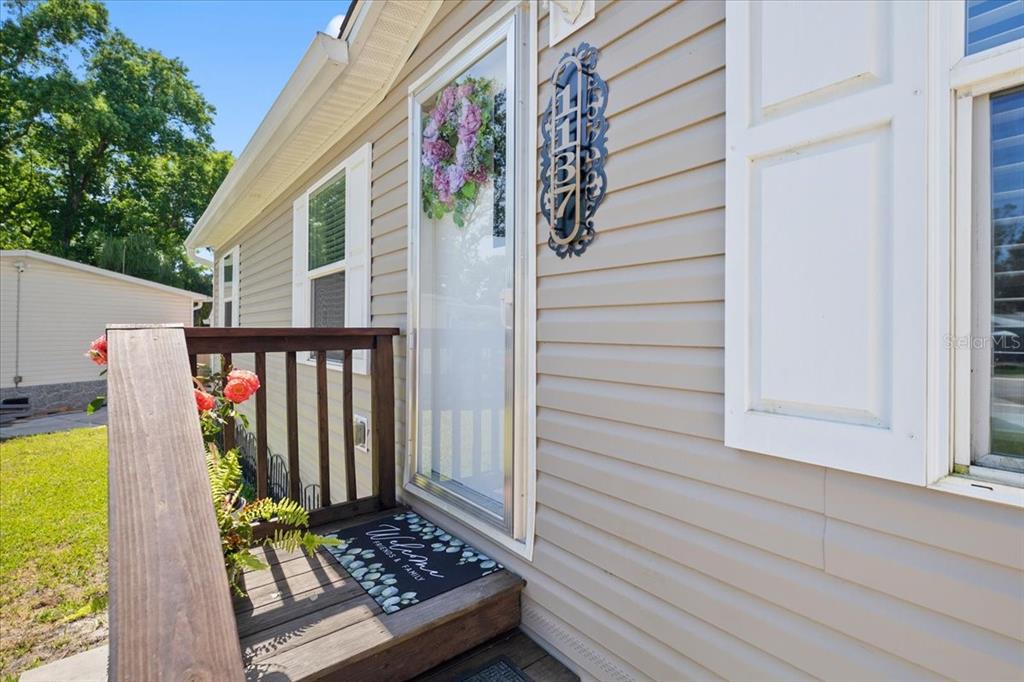 A wooden porch with a welcome mat leads to a house entrance with beige siding — 1137 YAUPON STREET, DAYTONA BEACH, FL