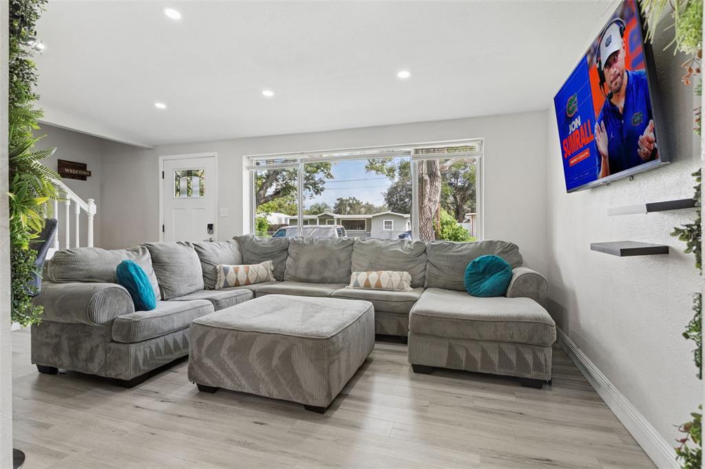 A living room features a large gray sectional sofa, light wood flooring, and a wall-mounted television — 4012 W FAIRVIEW HEIGHTS, TAMPA, FL