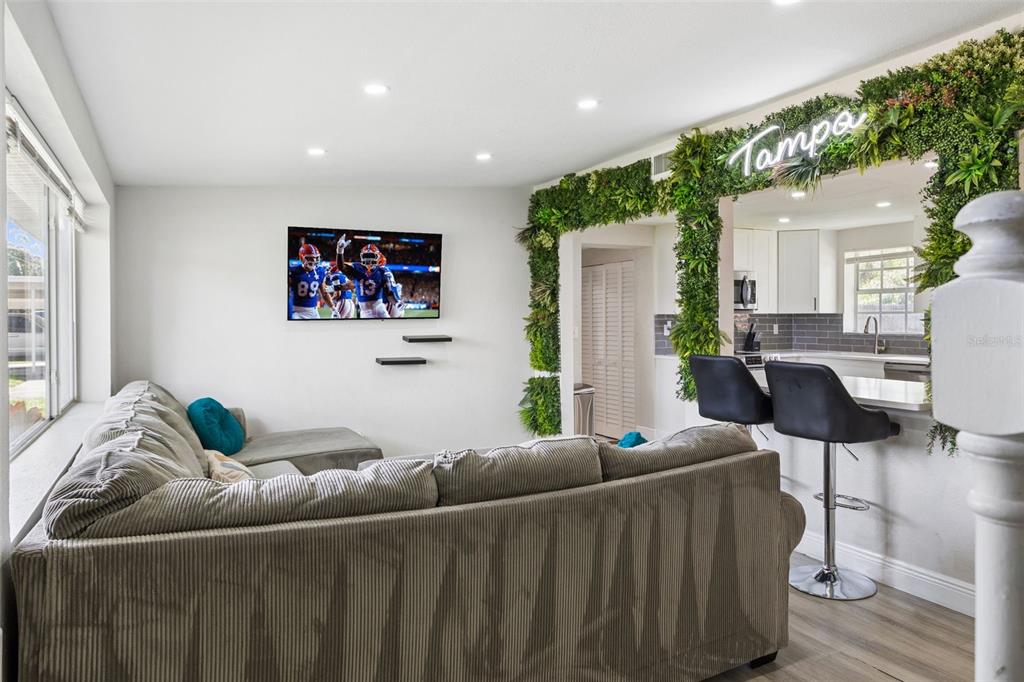 A living room features a grey sectional sofa, a wall-mounted television, and a faux-plant archway — 4012 W FAIRVIEW HEIGHTS, TAMPA, FL
