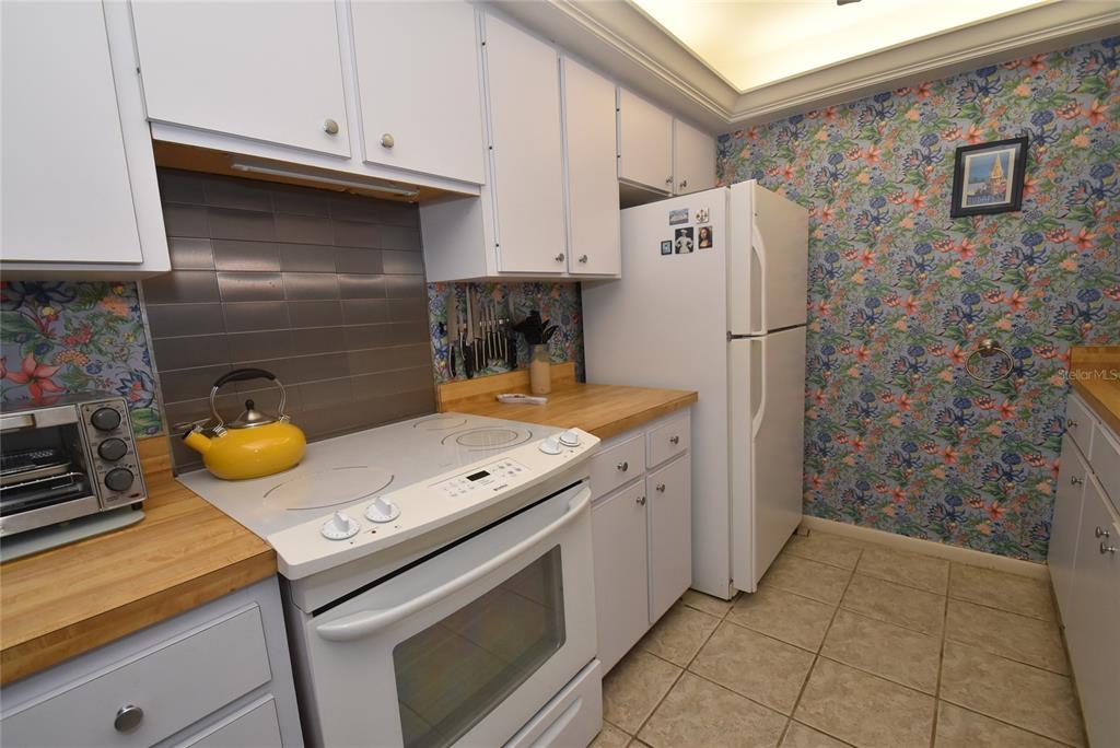 A kitchen features white cabinets, a white stove, a refrigerator, and floral wallpaper — 1703 PELICAN COVE ROAD UNIT GL356, SARASOTA, FL