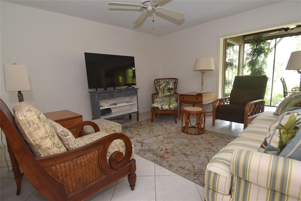 A living room features a ceiling fan, a television, and various seating options on tile — 1703 PELICAN COVE ROAD UNIT GL356, SARASOTA, FL
