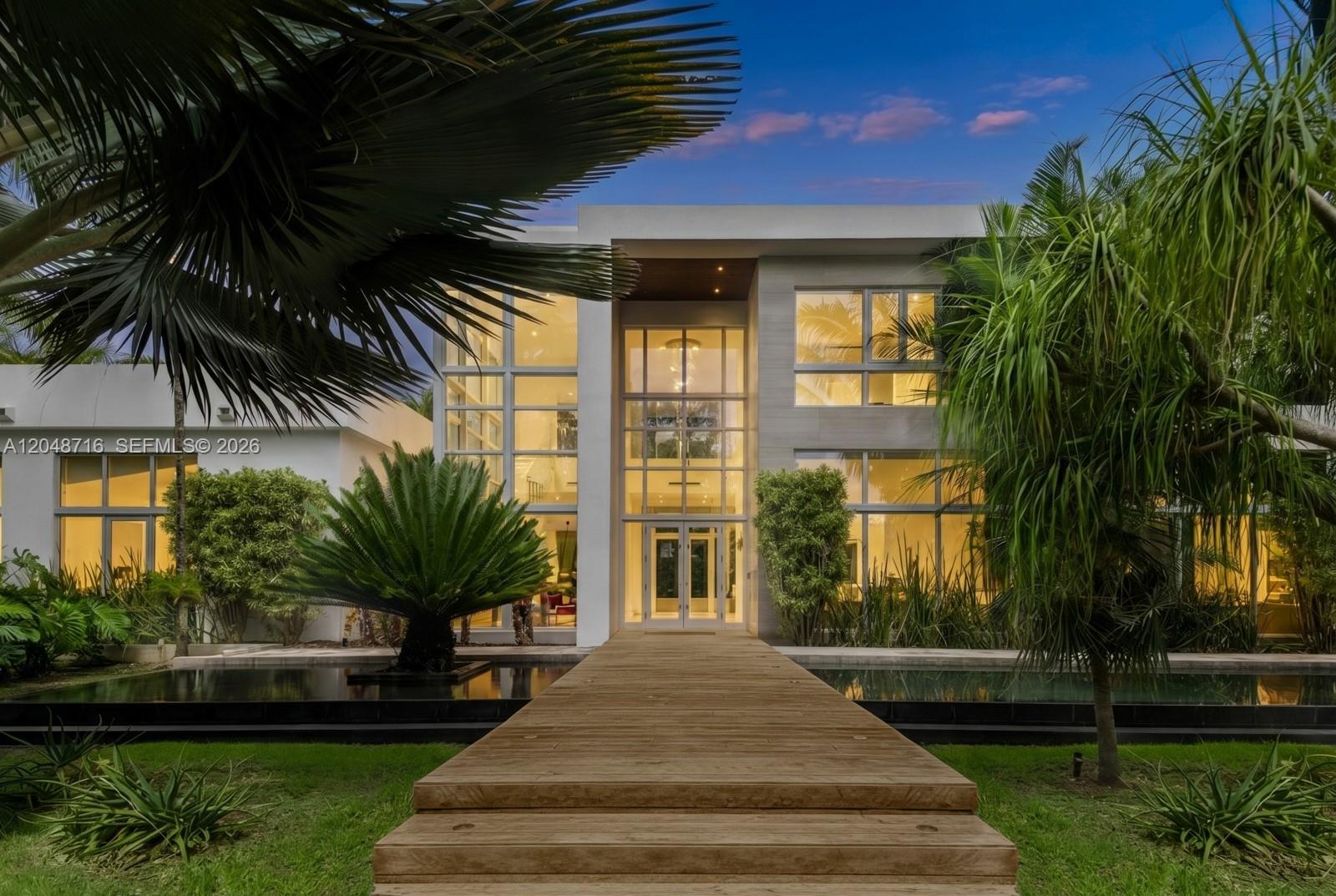 A modern two-story house features a wooden walkway leading to a glass-paneled entrance over water — 12900 SW 63rd Ave, Pinecrest FL 33156, PINECREST, FL