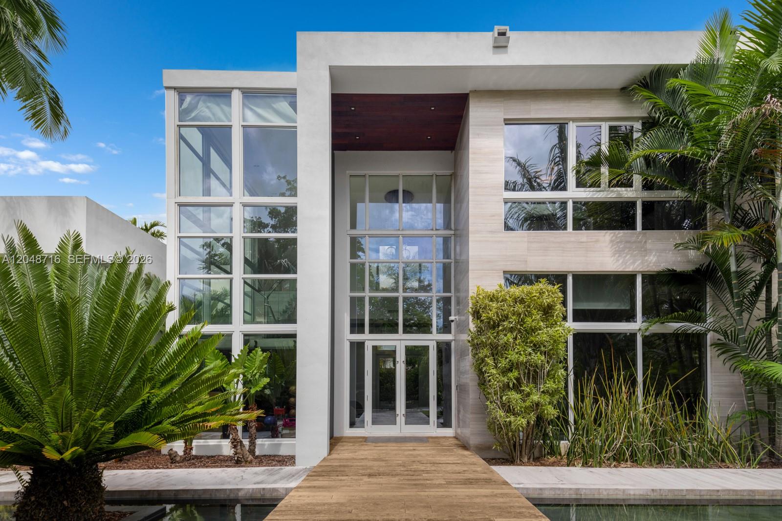A modern two-story house features a glass entryway, wood walkway, and surrounding tropical landscaping — 12900 SW 63rd Ave, Pinecrest FL 33156, PINECREST, FL