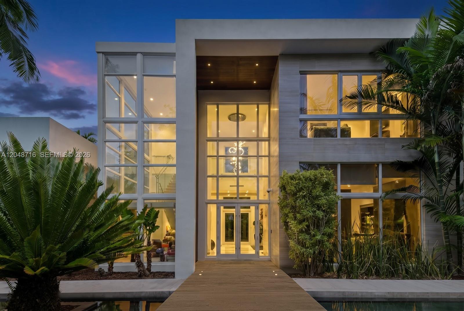 A modern two-story house exterior features a glass entryway, wooden walkway, and surrounding palm trees — 12900 SW 63rd Ave, Pinecrest FL 33156, PINECREST, FL