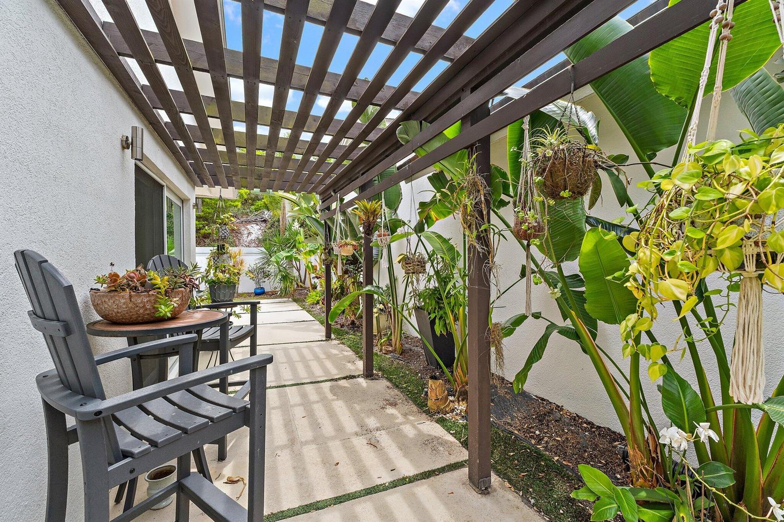 A covered outdoor patio features a wooden pergola, concrete pavers, and various potted hanging plants — 126 Seashore Drive, Jupiter FL 33477, JUPITER, FL