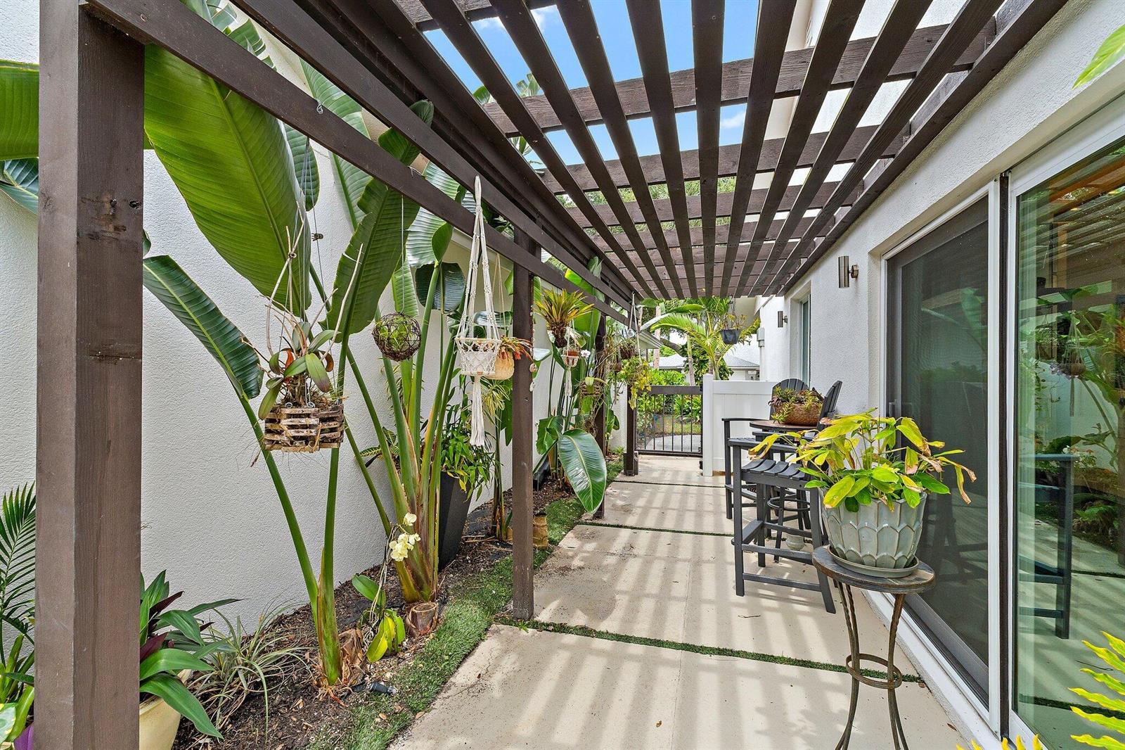 A narrow patio features a wooden pergola, potted plants, and a small bistro table set — 126 Seashore Drive, Jupiter FL 33477, JUPITER, FL