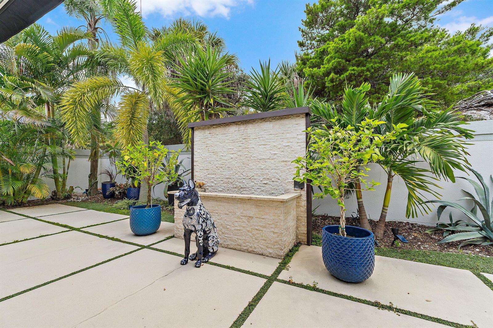 A stone water feature stands on a paved patio surrounded by potted plants and palms — 126 Seashore Drive, Jupiter FL 33477, JUPITER, FL