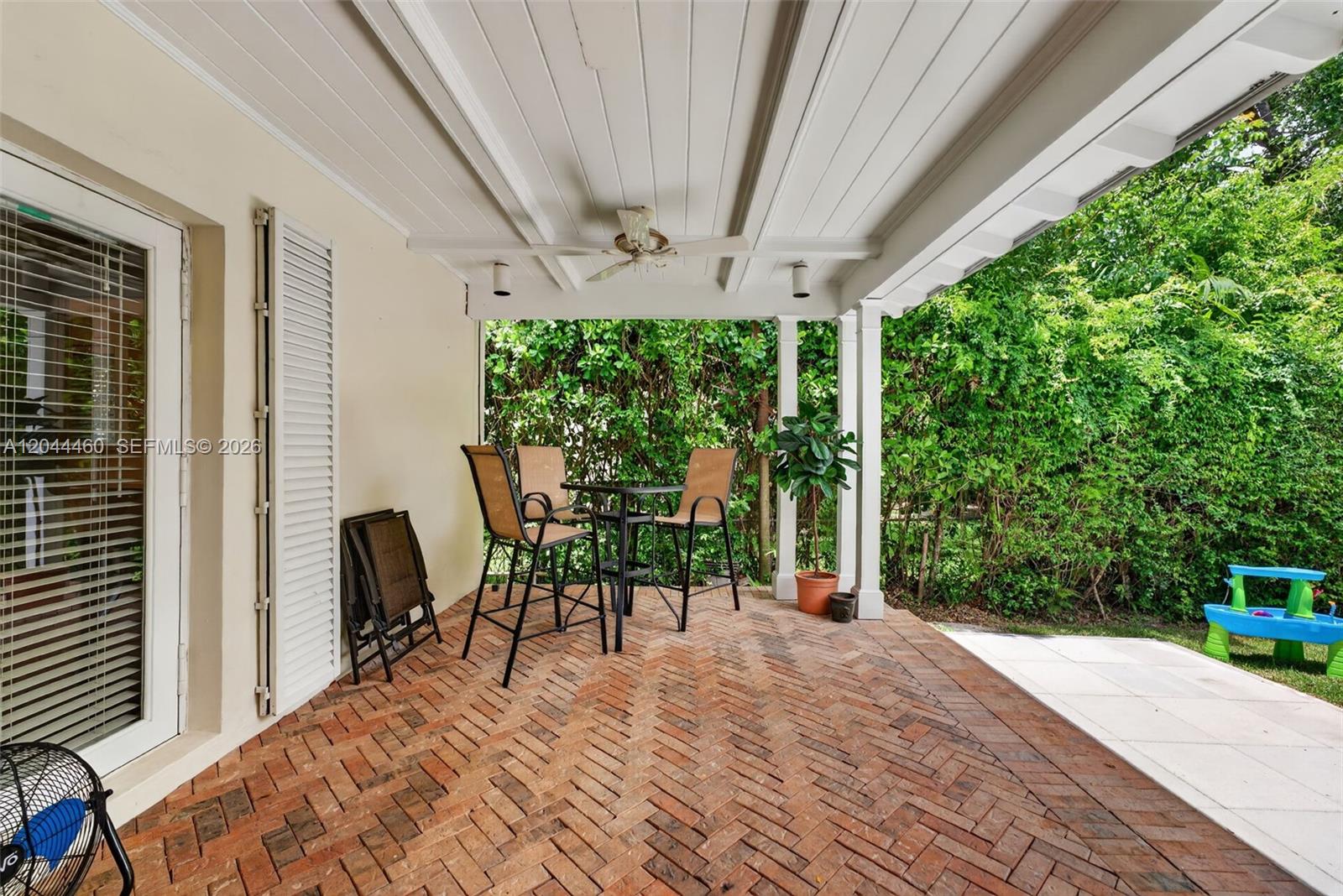 A covered patio features a herringbone brick floor, a dining set, and lush greenery — 1710 Segovia St, Coral Gables FL 33134, CORAL GABLES, FL