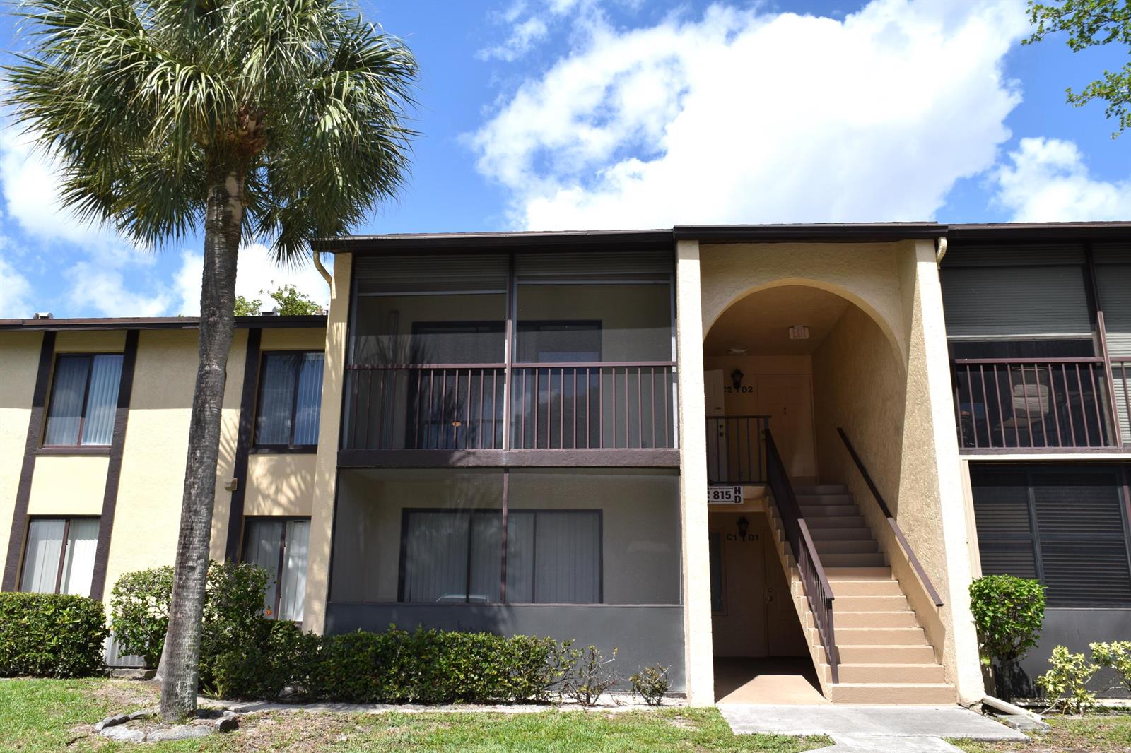 A two-story apartment building features a palm tree, screened balconies, and an exterior staircase — 815 Sky Pine Way # C2, FL 33415, FL