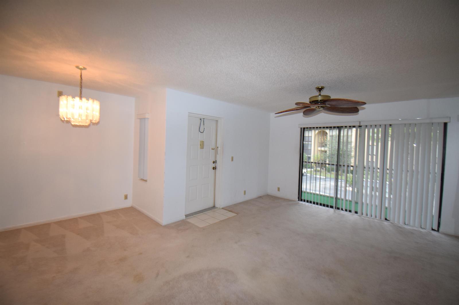 An empty living room with beige carpet, a ceiling fan, and a sliding glass door — 815 Sky Pine Way # C2, FL 33415, FL