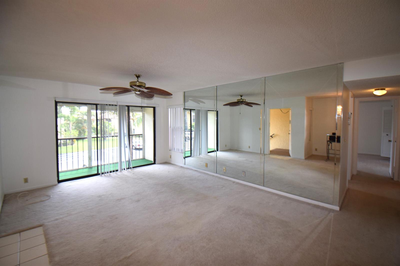 A living room with beige carpeting, a ceiling fan, and a large mirrored accent wall — 815 Sky Pine Way # C2, FL 33415, FL