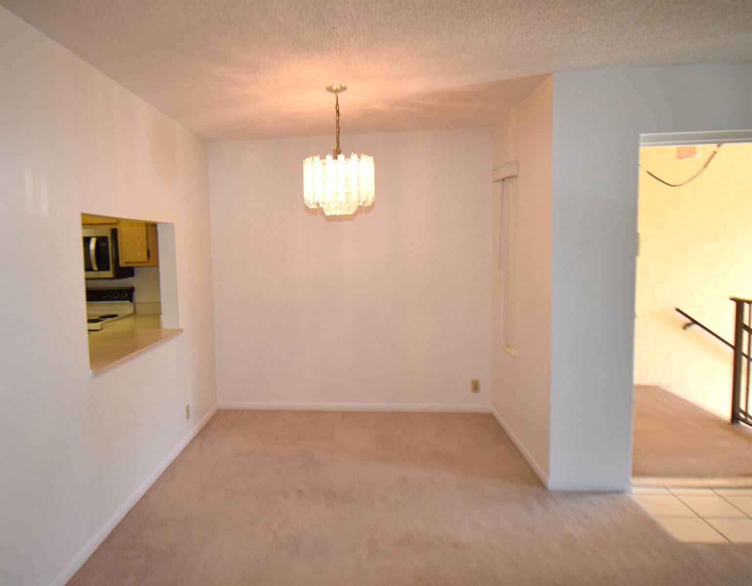 A dining area with beige carpet, a crystal chandelier, and a pass-through to the kitchen — 815 Sky Pine Way # C2, FL 33415, FL