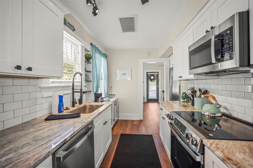 A galley kitchen features white cabinets, granite countertops, stainless steel appliances, and subway tile backsplashes — 634 6TH STREET N, ST PETERSBURG, FL