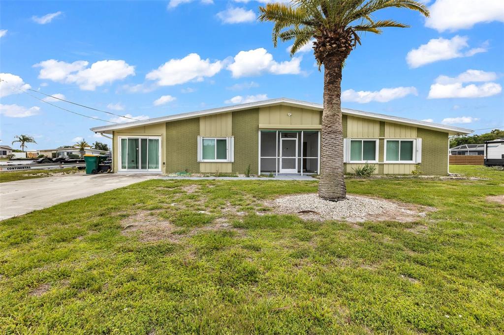 A single-story house with green siding, a palm tree, and a screened-in front entrance — 5527 FAIRWAY DRIVE S, PUNTA GORDA, FL