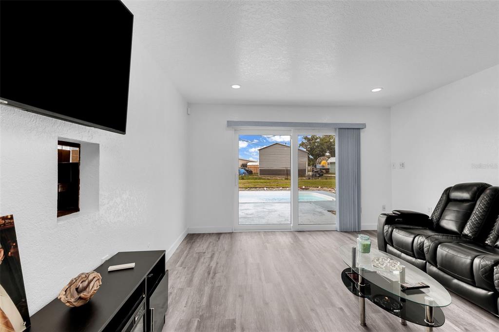A living room with light wood-look flooring, a black leather sofa, and a sliding glass door — 5527 FAIRWAY DRIVE S, PUNTA GORDA, FL