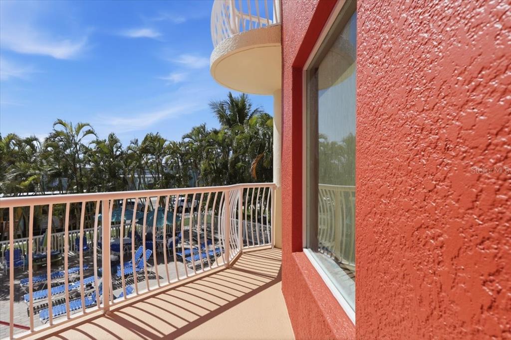 A balcony with white railings overlooks a pool area next to a textured red wall — 11605 GULF BOULEVARD UNIT 206, TREASURE ISLAND, FL