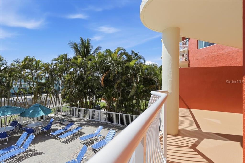 A view from a balcony overlooking a pool deck with lounge chairs and palm trees — 11605 GULF BOULEVARD UNIT 206, TREASURE ISLAND, FL