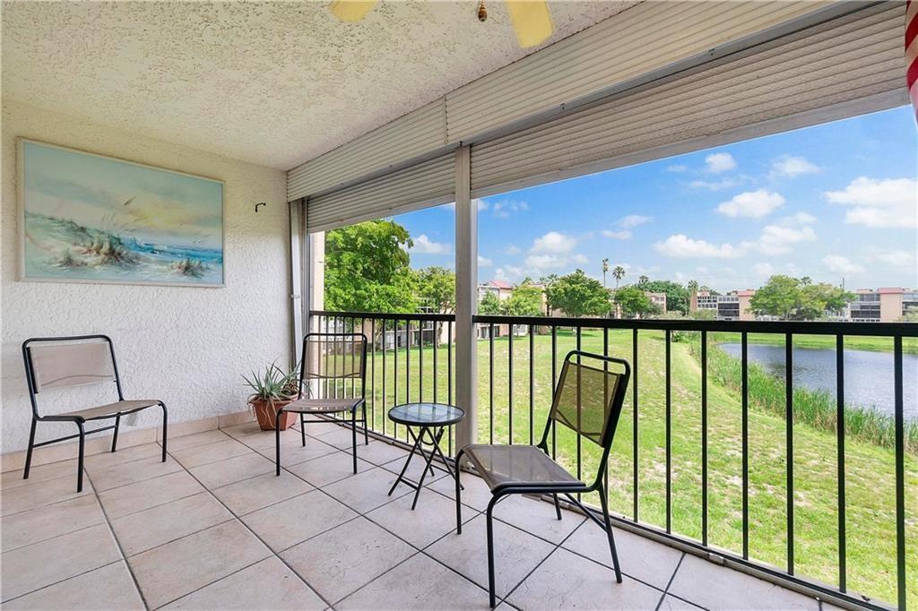 A tiled balcony features three chairs, a small table, and a view of a pond — 7210 Lake Circle Drive # 306, Margate FL 33063, MARGATE, FL