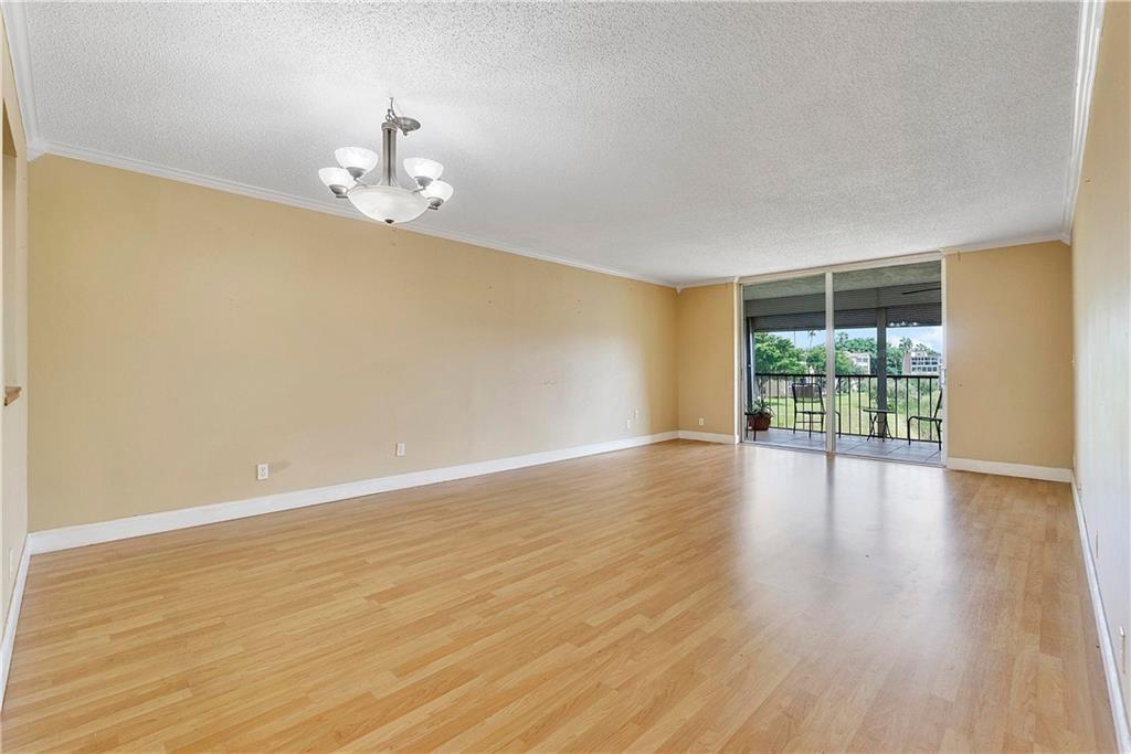 An empty living room features light wood laminate flooring, beige walls, and a sliding glass door — 7210 Lake Circle Drive # 306, Margate FL 33063, MARGATE, FL