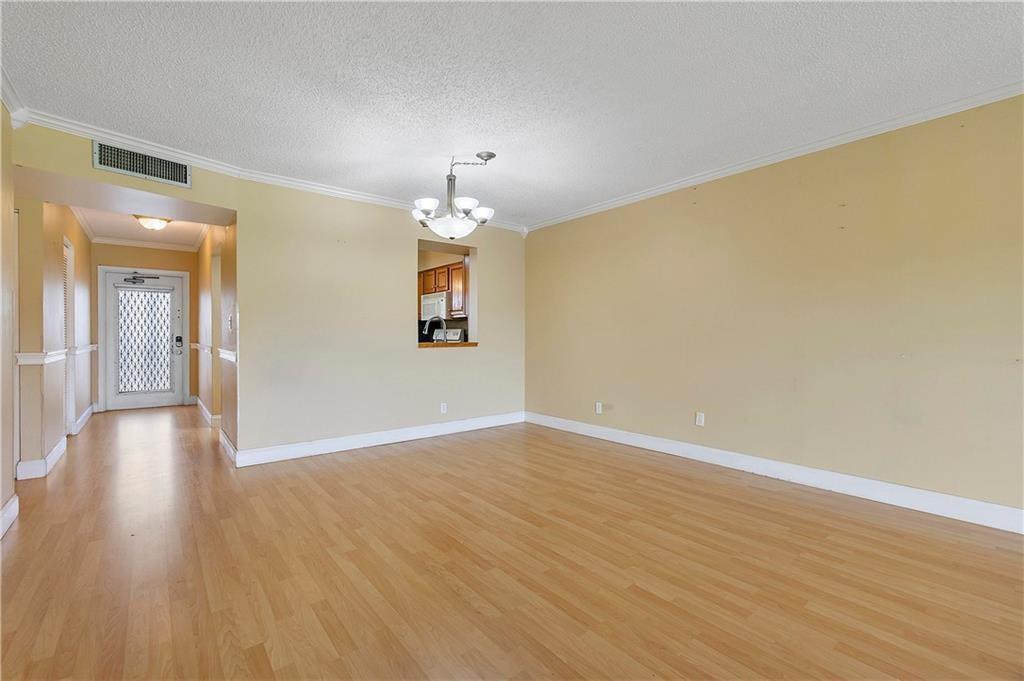 An empty room with light wood flooring, yellow walls, and a central chandelier — 7210 Lake Circle Drive # 306, Margate FL 33063, MARGATE, FL