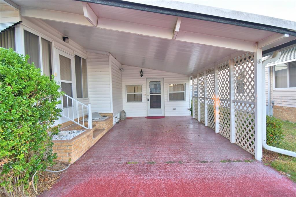 A covered carport with a red concrete floor, white lattice siding, and a brick entrance — 4251 CEDARWOOD STREET, WINTER HAVEN, FL
