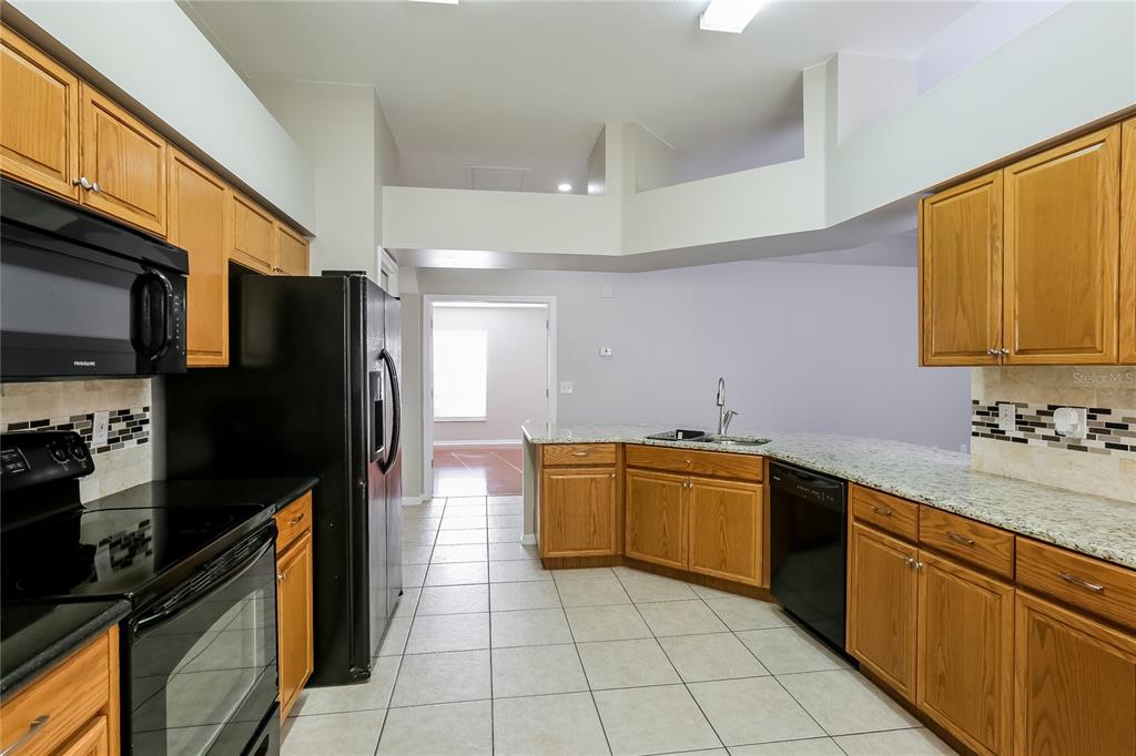 A kitchen features oak cabinets, black appliances, granite countertops, and light-colored tile flooring — 1717 ERIN BROOKE DRIVE, VALRICO, FL