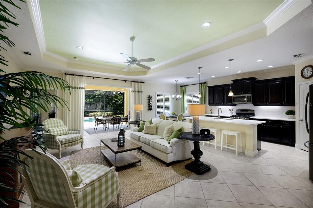 An open-concept living room and kitchen featuring a tray ceiling, tile floors, and patio access — 12109 WHISPER LAKE DRIVE, BRADENTON, FL