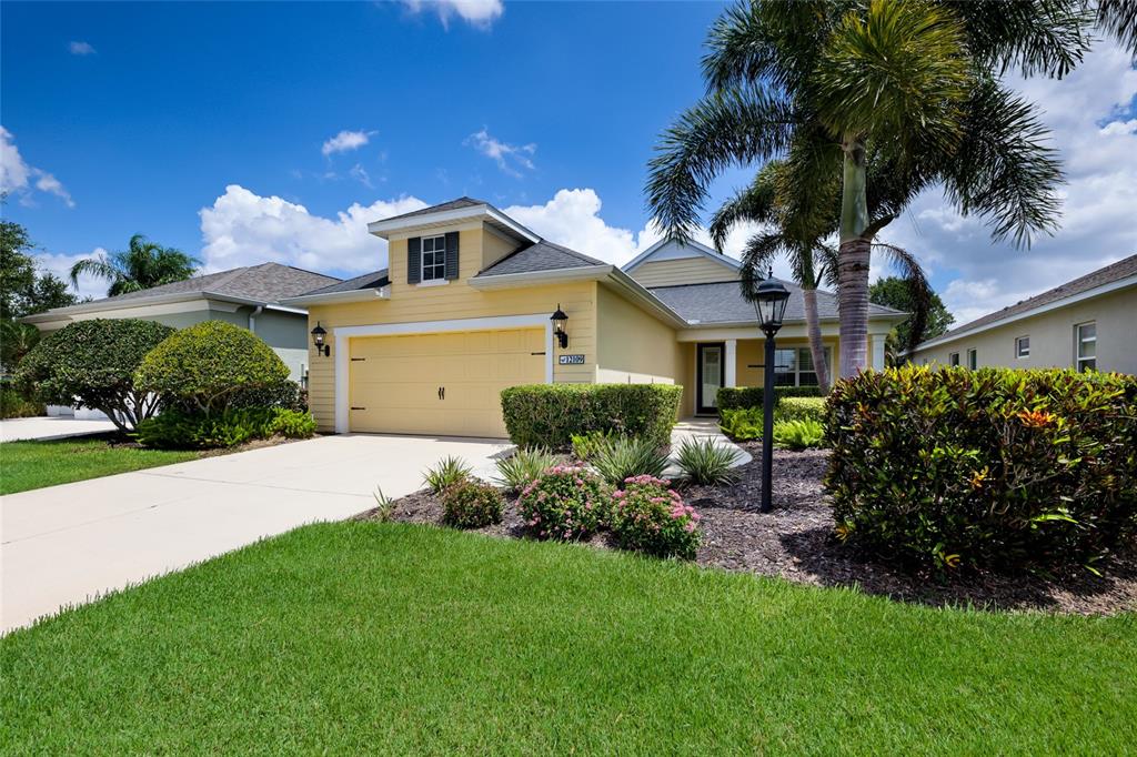 A yellow single-story house with a two-car garage, palm tree, and landscaped front yard — 12109 WHISPER LAKE DRIVE, BRADENTON, FL