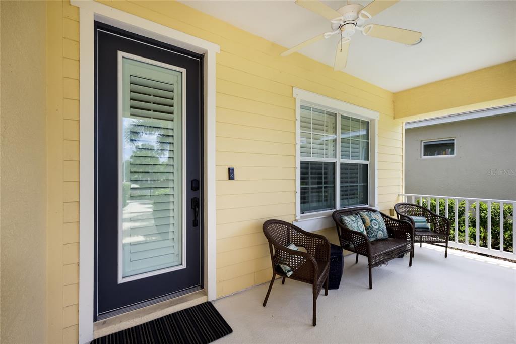 A yellow-sided porch features a dark front door, a ceiling fan, and three wicker chairs — 12109 WHISPER LAKE DRIVE, BRADENTON, FL