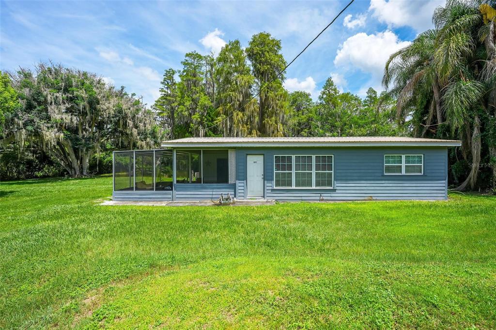 A blue single-story house with a screened-in porch sits on a large, grassy lawn — 10112 STATE ROAD 33, GROVELAND, FL