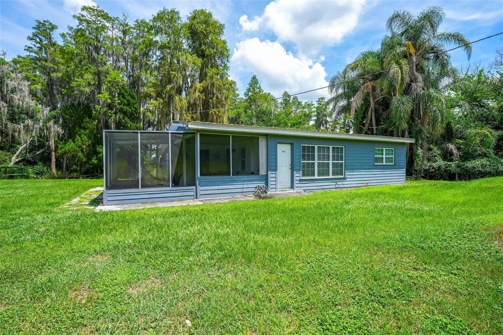 A blue single-story house with a screened-in porch sits on a grassy lot with trees — 10112 STATE ROAD 33, GROVELAND, FL