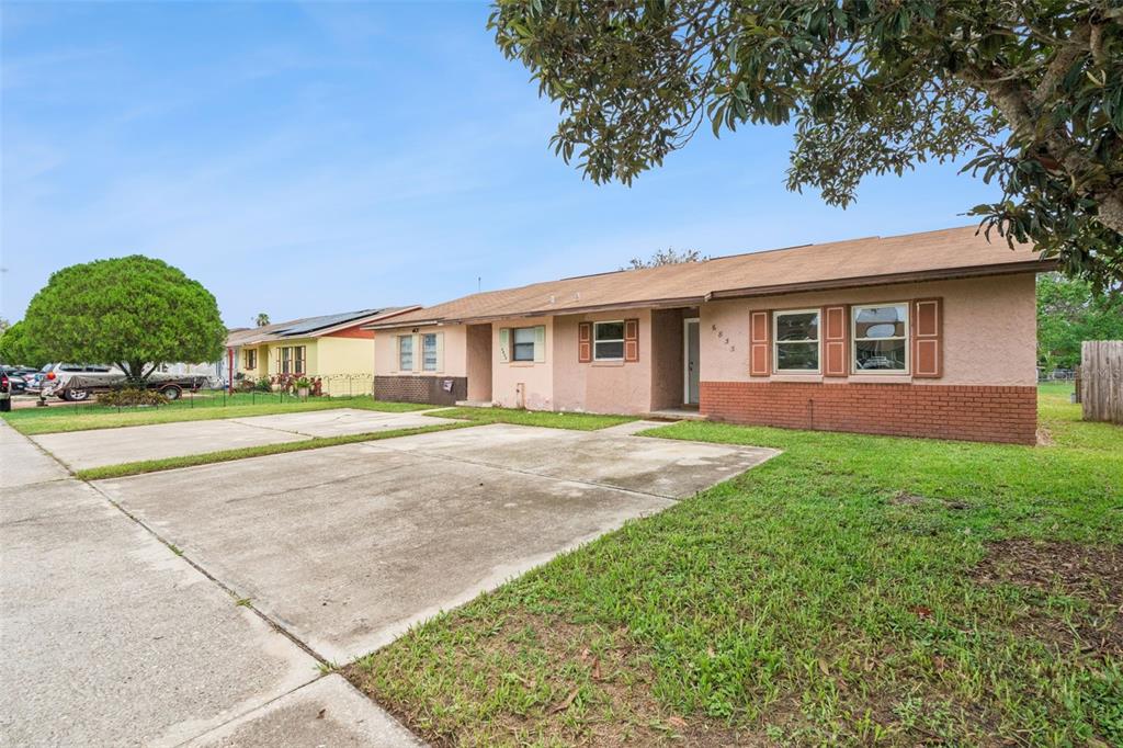 A single-story house with a tan stucco exterior, brick accents, and a large concrete driveway — 6835 LONGMEADE LANE, ORLANDO, FL