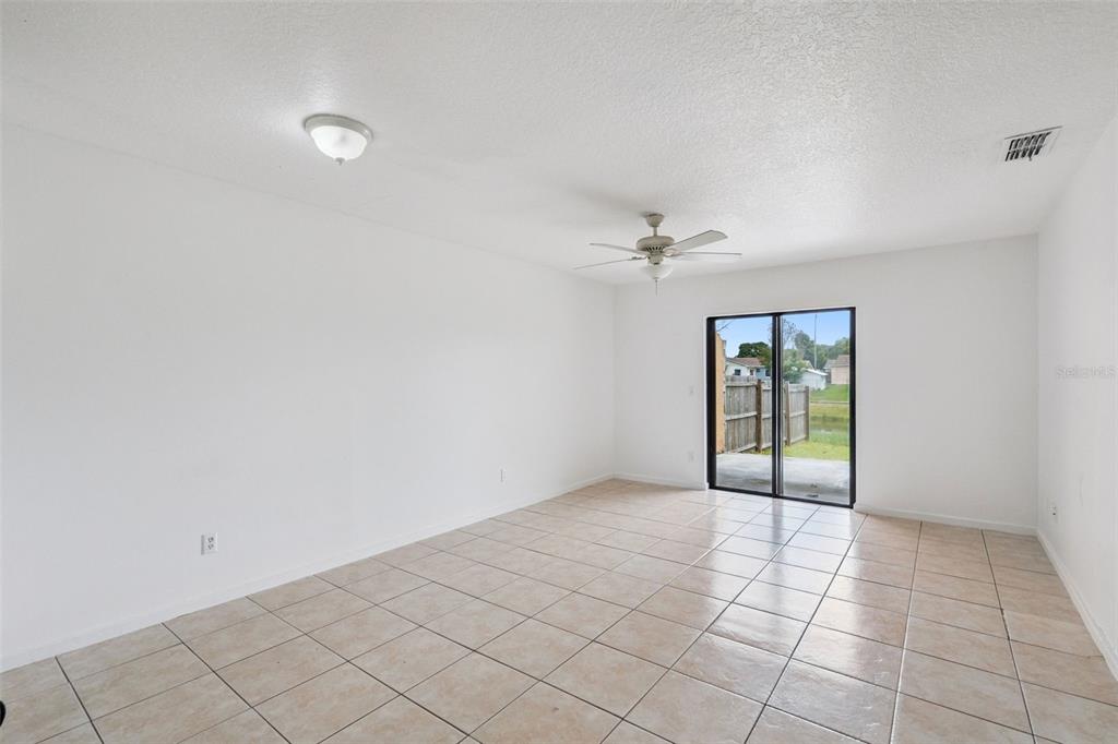 An empty room with white walls, beige tile flooring, a ceiling fan, and sliding doors — 6835 LONGMEADE LANE, ORLANDO, FL
